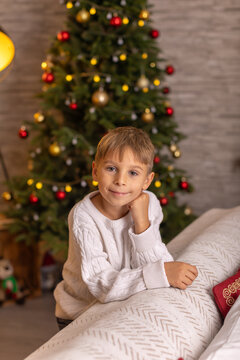 Cute preschool boy, sitting in front of the fireplace, holding christmas present and reading a book, joy and happiness