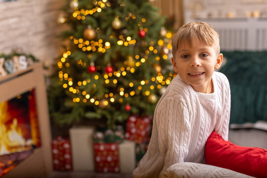 Cute preschool boy, sitting in front of the fireplace, holding christmas present and reading a book, joy and happiness