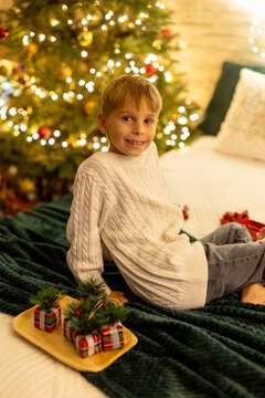 Cute preschool boy, sitting in front of the fireplace, holding christmas present and reading a book, joy and happiness