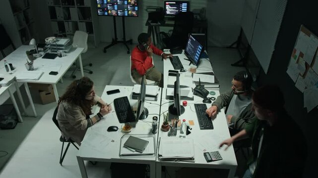 Diverse multiethnic young team working at desktop computers wearing headsets in scam office, top view. Suitable for scam awareness