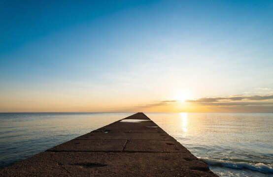 Concrete breakwater pier stretching into a calm sea at sunset