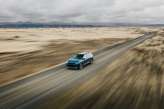 Aerial view of a blue SUV driving on a gravel road through the vast and desolate landscape near Hlidarvatn, Sveitarfelagid Olfus, Iceland.