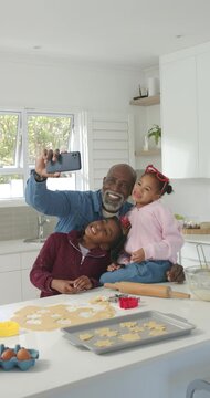 Vertical video: Grandpa holding phone taking selfies with child granddaughters baking in kitchen