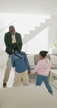 Vertical video: African man leading play gesturing as 2 child girls mirroring at home near sofa