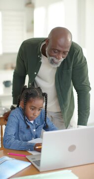 Vertical video: African American senior man leaning, helping child typing on laptop in home