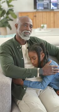 Vertical video: Senior African American man holding child on sofa after child resting head