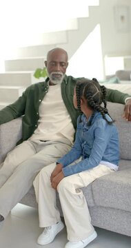 Vertical video: African senior man and youth girl on sofa at home girl turning talking connecting