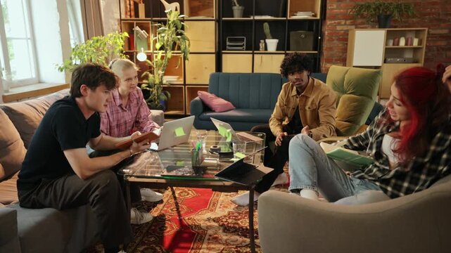 Young man displays laptop to coworkers during informal meeting with persuasive enthusiasm. Online teamwork, idea presentation, digital collaboration concept