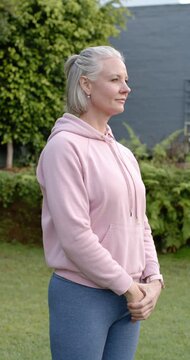 Vertical video: Middle-aged woman in garden with pink hoodie, moving from clasped hands to smiling