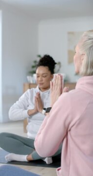 Vertical video: Senior woman guiding African American woman breathing on yoga mats at home to relax