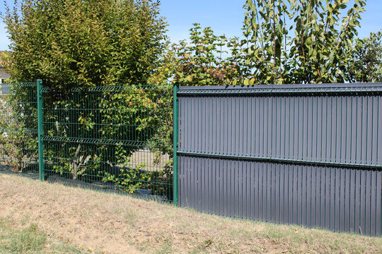 Transition entre grillage rigide nu vert et panneau avec lattes occultantes anthracite sur un terrain en pente