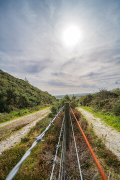 Pathway along fence line with barbed wire leading towards landscape in Cornwall
