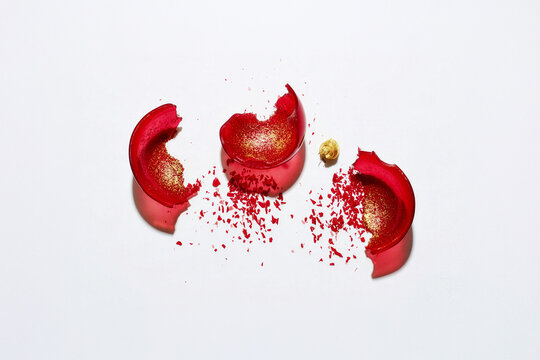Fragments of a shattered red ornament scattered across a white surface