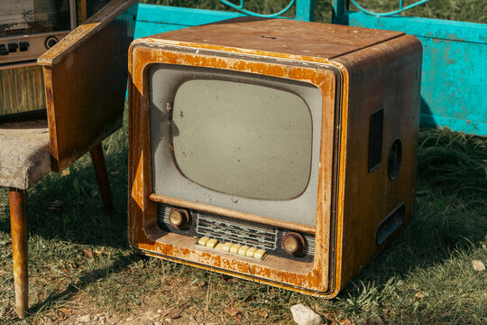 weathered vintage Soviet-era wooden cabinet television set with a CRT screen and tuning knobs stands on green grass in sunny outdoor lighting.