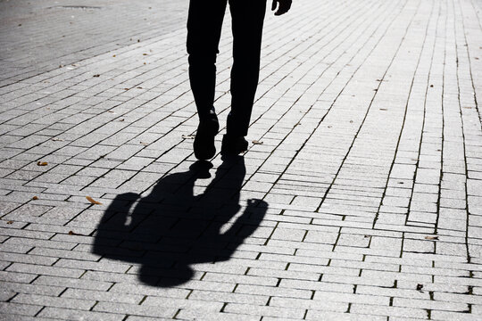 Black silhouette and shadow of lonely man walking on a street. Male legs on sidewalk at autumn