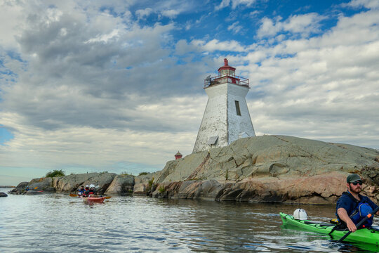 Sea kayakers paddle beneath the historic Bustard Rocks lighthouse on a granite island, copy space, French River, Georgian Bay, Ontario, Canada