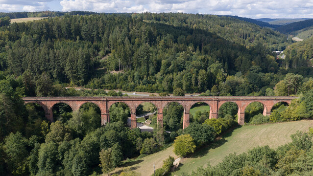 Aerial view of the historic red sandstone Himbaechel Viaduct spanning a lush green valley with dense forests and rolling hills in Erbach, Hessen, Germany.