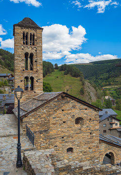Medieval Romanesque church of Sant Climent de Pal in Andorra with stone bell tower, green mountain valley, pine forest and blue sky with white clouds