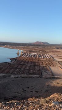 Panoramic view of Las Salinas de Janubio in Lanzarote, Canary Islands, Spain. The image showcases the historic salt flats, calm lagoon, traditional windmills, and volcanic hills, highlighting one of t