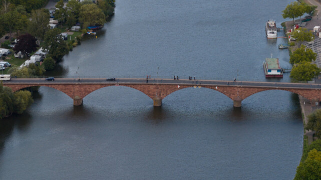 Aerial view of the Mainbrucke stone arch bridge spanning the Main river, with cars and pedestrians crossing, surrounded by trees and boats in Miltenberg, Bayern, Germany.