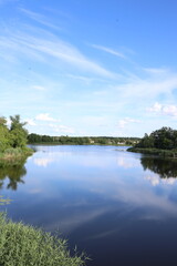 Obraz premium Clear water reflects cloudy sky over calm river near trees
