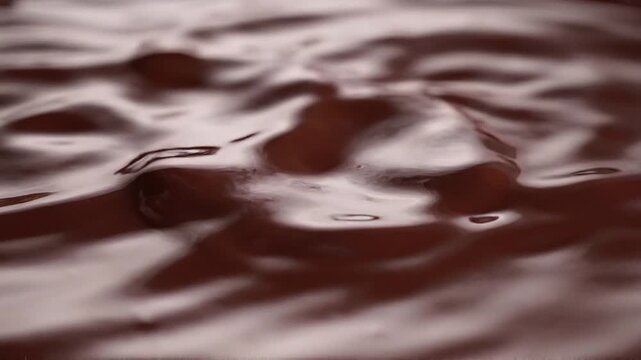 Liquid dark chocolate ripple surface close-up: smooth melted cocoa background texture