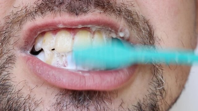 Man brushing his teeth with a blue toothbrush with foam, close-up. Man taking care of his oral cavity by brushing his teeth with toothpaste and brush. Hygiene, daily self-care and dental health