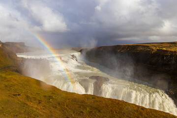 Beautiful panoramic view of powerful Gullfoss waterfall cascades with a bright rainbow under dramatic stormy clouds, Iceland © olyasolod