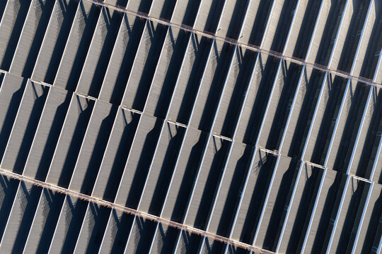Aerial view of a large warehouse roof with repeating geometric patterns and long shadows cast across the industrial metal structure in Warsaw, Masovian Voivodeship, Poland.