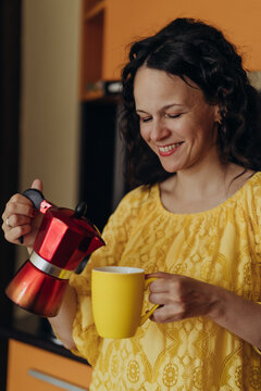 Smiling woman pours fresh coffee from moka pot into yellow mug in home kitchen creating scene about home brewing coffee culture mindful consumption slow living and affordable daily rituals at home.