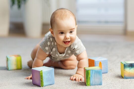 Happy baby crawling among colorful building blocks indoors