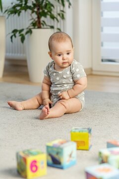 Sad baby sitting on carpet near colorful blocks indoors