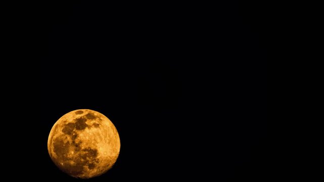 Large orange full moon moving across the dark night sky. Timelapse of a full moon moving across the dark night sky