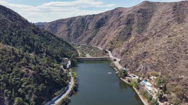 High angle drone shot over San Roque lake approaching dam wall between mountains