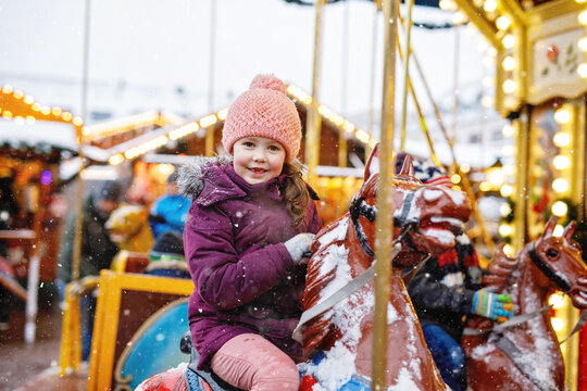 Adorable little girl riding merry-go-round carousel horse at Christmas funfair outdoors. Happy child enjoying traditional family Xmas market in Nuremberg, Germany