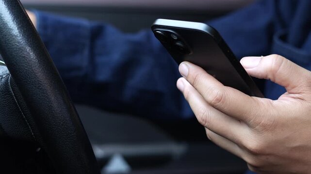 Close up of hands holding a smart phone at a car steering wheel, illustrating distracted driving, mobile phone use and road safety risks.