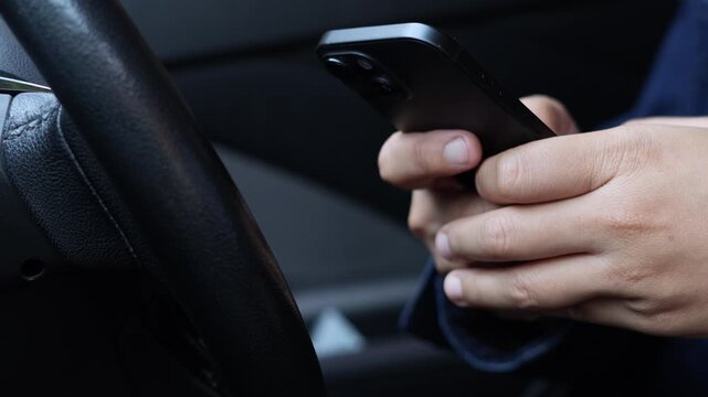 Close up of hands holding a smart phone at a car steering wheel, illustrating distracted driving, mobile phone use and road safety risks.