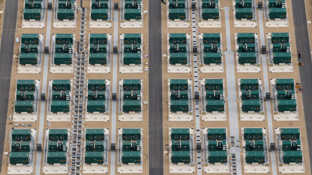 Aerial view of a large-scale battery energy storage system with rows of green industrial containers on gravel pads and paved access paths in London, England, United Kingdom.