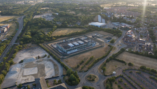 Aerial view of a modern data center facility surrounded by green fields, suburban housing, and road networks in Bracknell, England, United Kingdom.