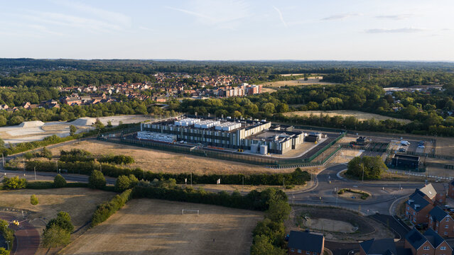 Aerial view of a modern data center facility surrounded by green fields, trees, and residential neighborhoods in Bracknell, England, United Kingdom.
