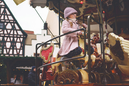 Little school girl riding on a merry go round carousel at Christmas funfair or market, outdoors. Happy child having fun on traditional family xmas market in Germany