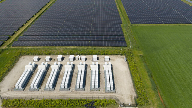 Aerial view of a large solar farm featuring rows of photovoltaic panels and white battery storage units situated in a rural landscape in Wanneperveen, Overijssel, Netherlands.