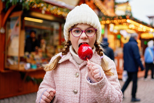 Little cute kid girl eat sweet sugar covered red candy apple on Christmas market. Happy child on traditional Xmas fair in Germany.