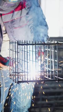 Worker in a welding helmet welding a rebar cage with bright sparks at a factory