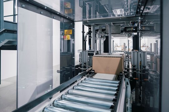Automated packaging line moving a cardboard box on a roller conveyor inside a modern industrial facility, showing automated packing, material handling, logistics and order fulfillment