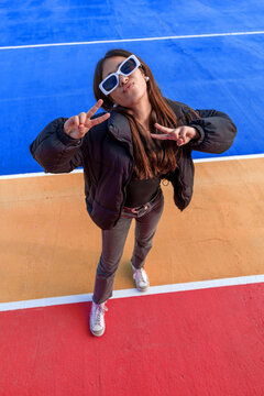 Young woman making peace signs, posing with confidence and individuality on colorful urban sports court