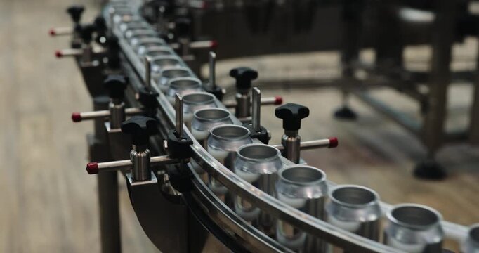 Empty metal cans travel around curved conveyor inside automated packaging plant. Precision guide rails maintain alignment during continuous factory transporting