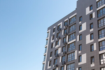 Fototapeta premium Modern apartment building facade with geometric design against clear blue sky emphasizing contemporary residential architecture, urban housing, real estate investment, sustainable city 