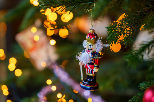 Close-up of Christmas ornament toys and balls hanging on a decorated tree with warm lights, festive tinsel and cozy holiday atmosphere at home.