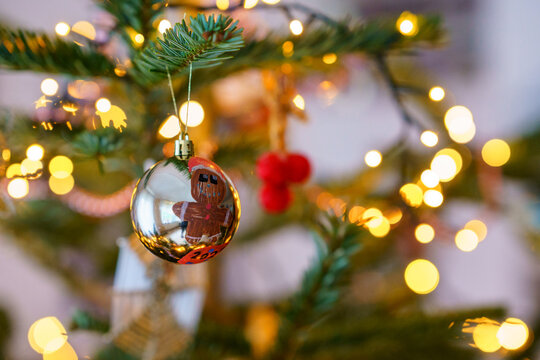 Close-up of Christmas ornament toys and balls hanging on a decorated tree with warm lights, festive tinsel and cozy holiday atmosphere at home.